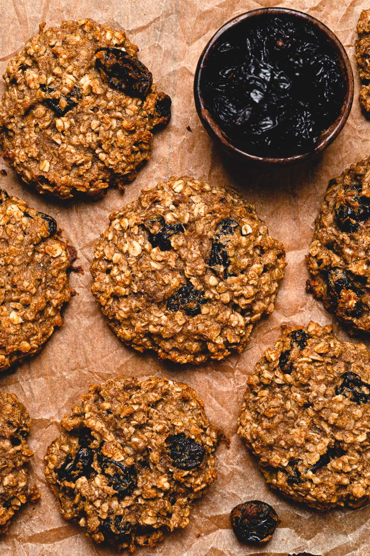 vegan breakfast cookies laid out on a sheet of parchment paper with a small bowl of raisins in the corner