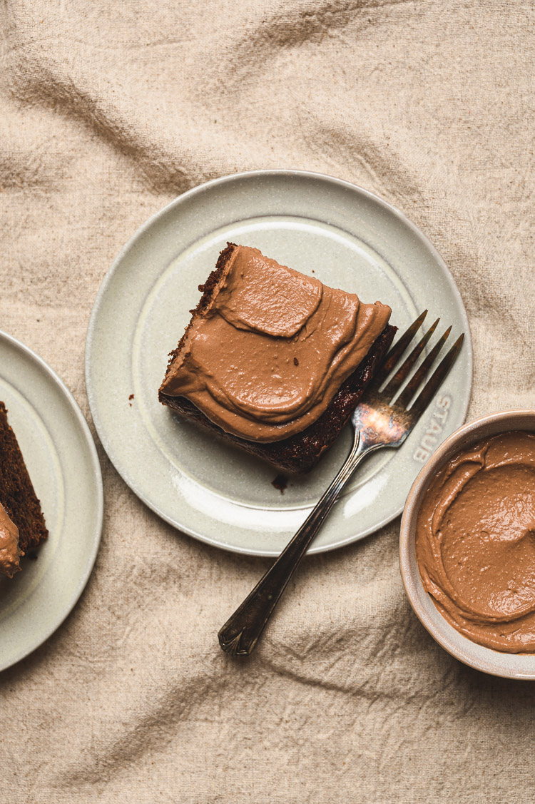 chocolate banana snack cake on dessert plates, bowl of frosting in the right corner