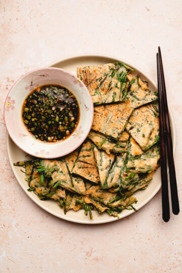 chive pancakes on a plate with a bowl of dipping sauce, chopsticks on the plate