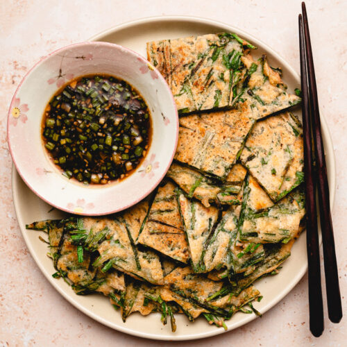 chive pancakes on a plate with a bowl of dipping sauce, chopsticks on the plate