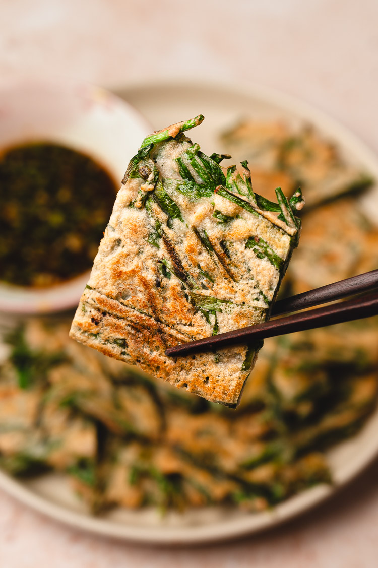 close up piece of chive pancake being held up with chopsticks