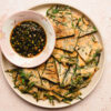 chive pancakes on a plate with dipping sauce in a bowl on the plate