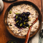 overnight oats in a bowl seen from overhead, topped with frozen blueberries and pumpkin seeds, spoon in bowl