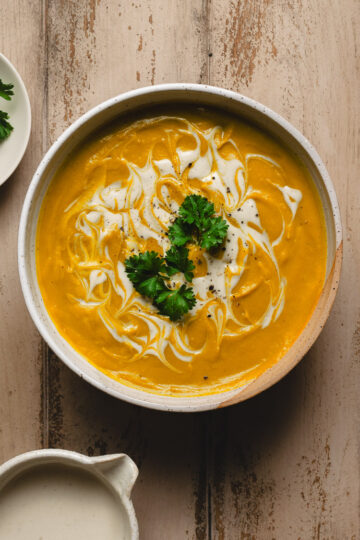 bowl of red lentil kabocha soup, cashew cream in small bowl below