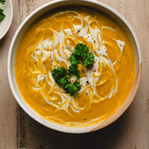 bowl of red lentil kabocha soup, cashew cream in small bowl below