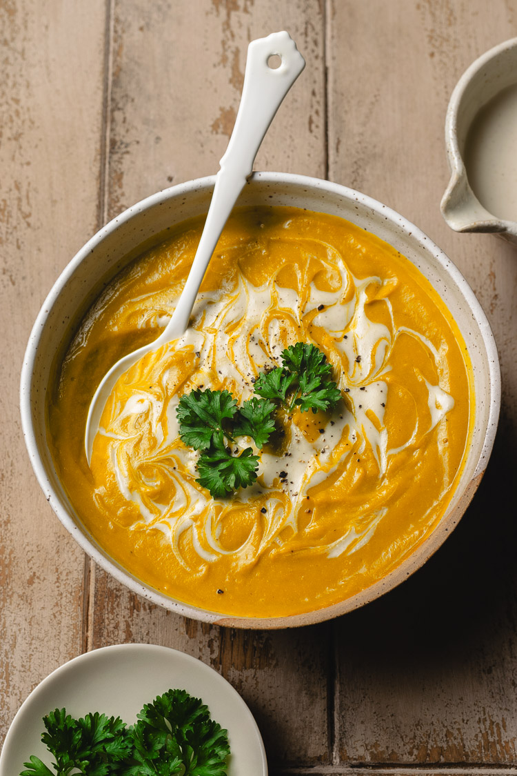 bowl of vegan kabocha soup, spoon in bowl, topped with parsley and swirls of cashew cream