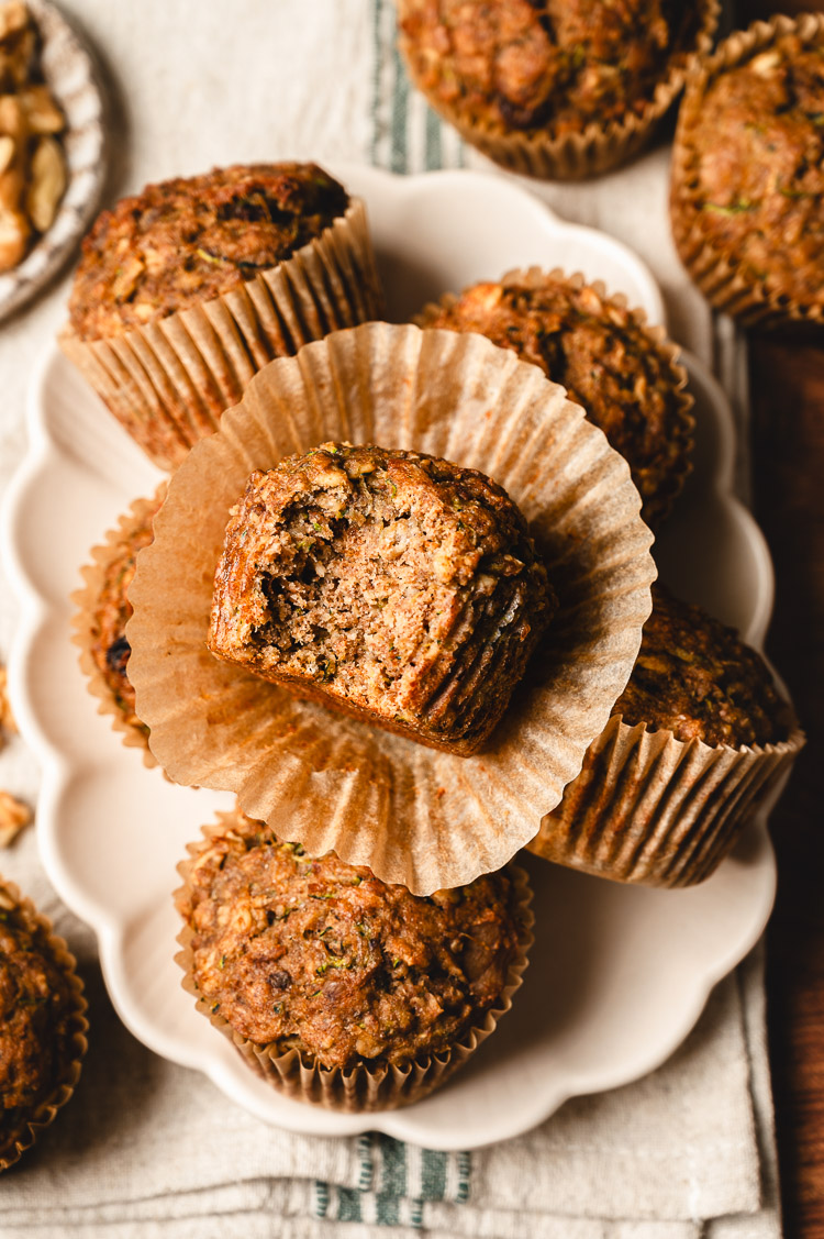 zucchini oatmeal muffins stacked on a plate with a bite taken out of top muffin