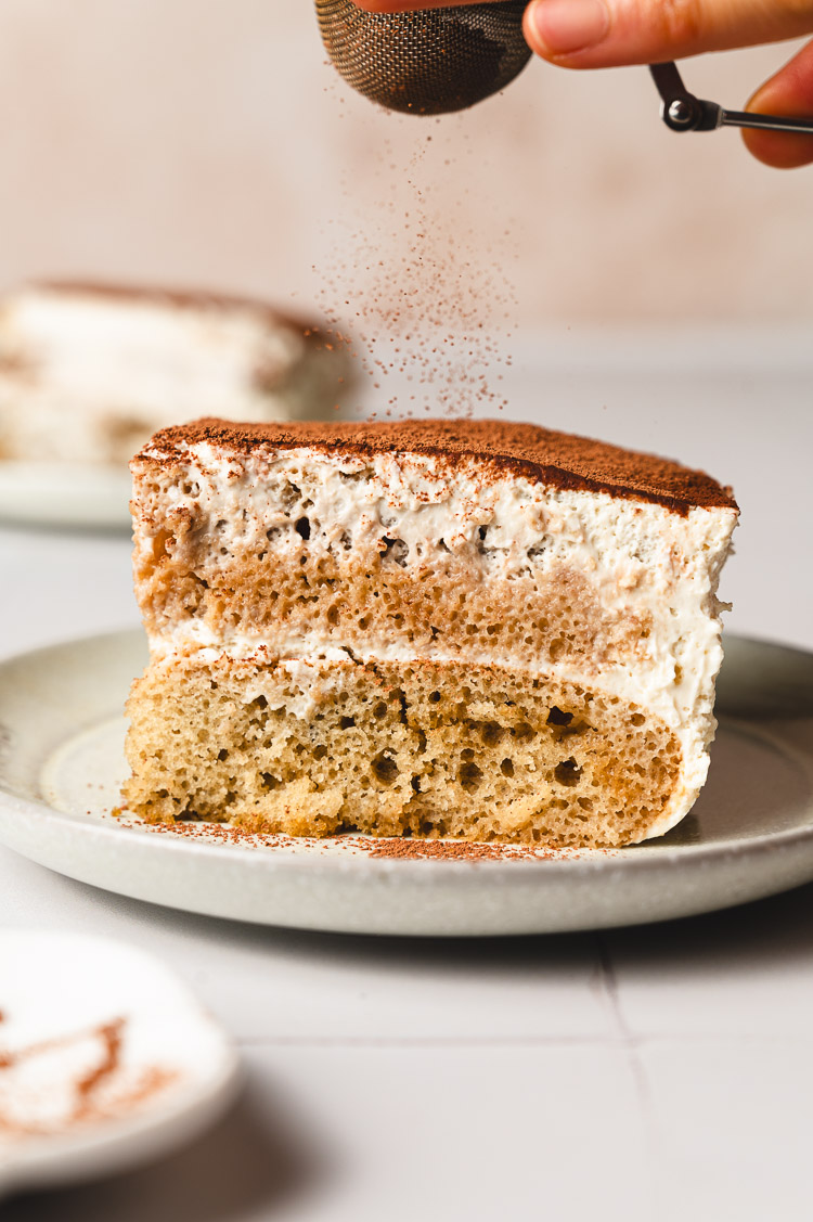 vegan tiramisu slice being dusted with cocoa powder