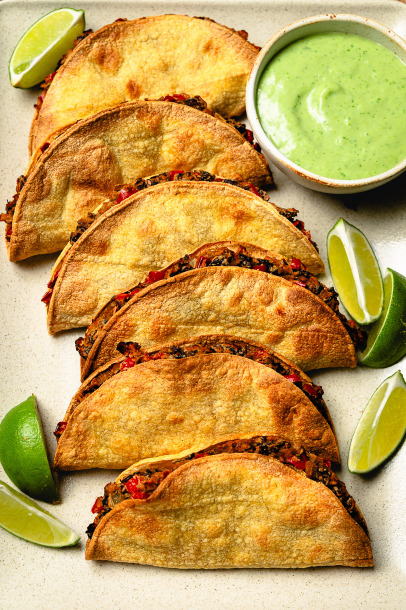 crispy black bean tacos on serving platter with small bowl of cilantro lime sauce